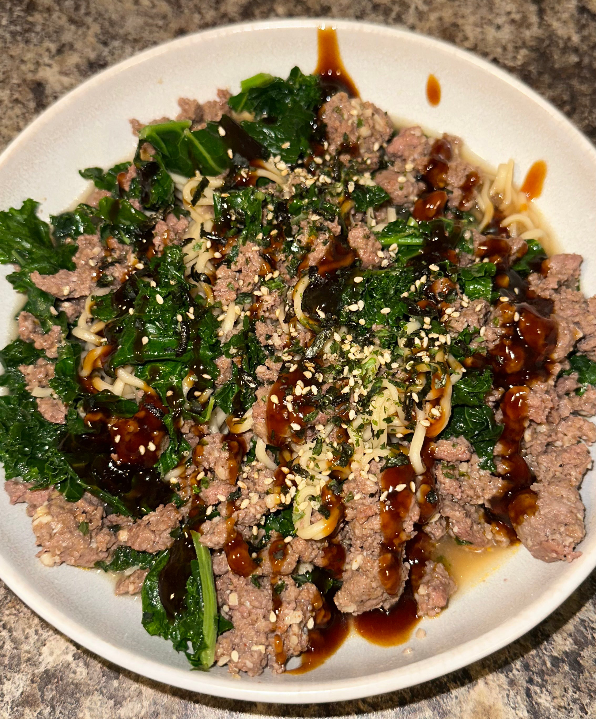 Plated dish of ground meat with greens and sauce on a white plate.
